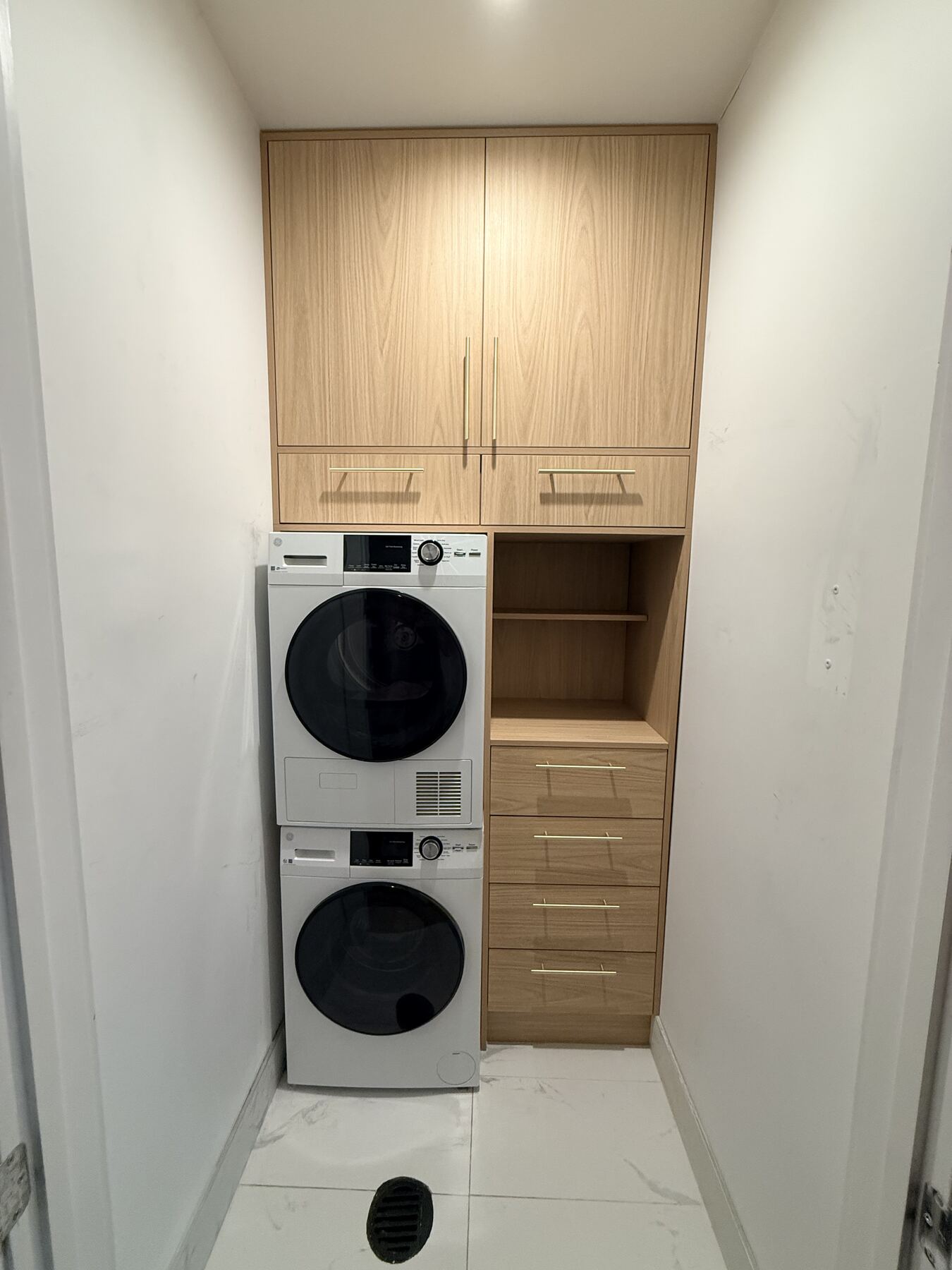 Laundry closet with stacked washer dryer and oak cabinetry
